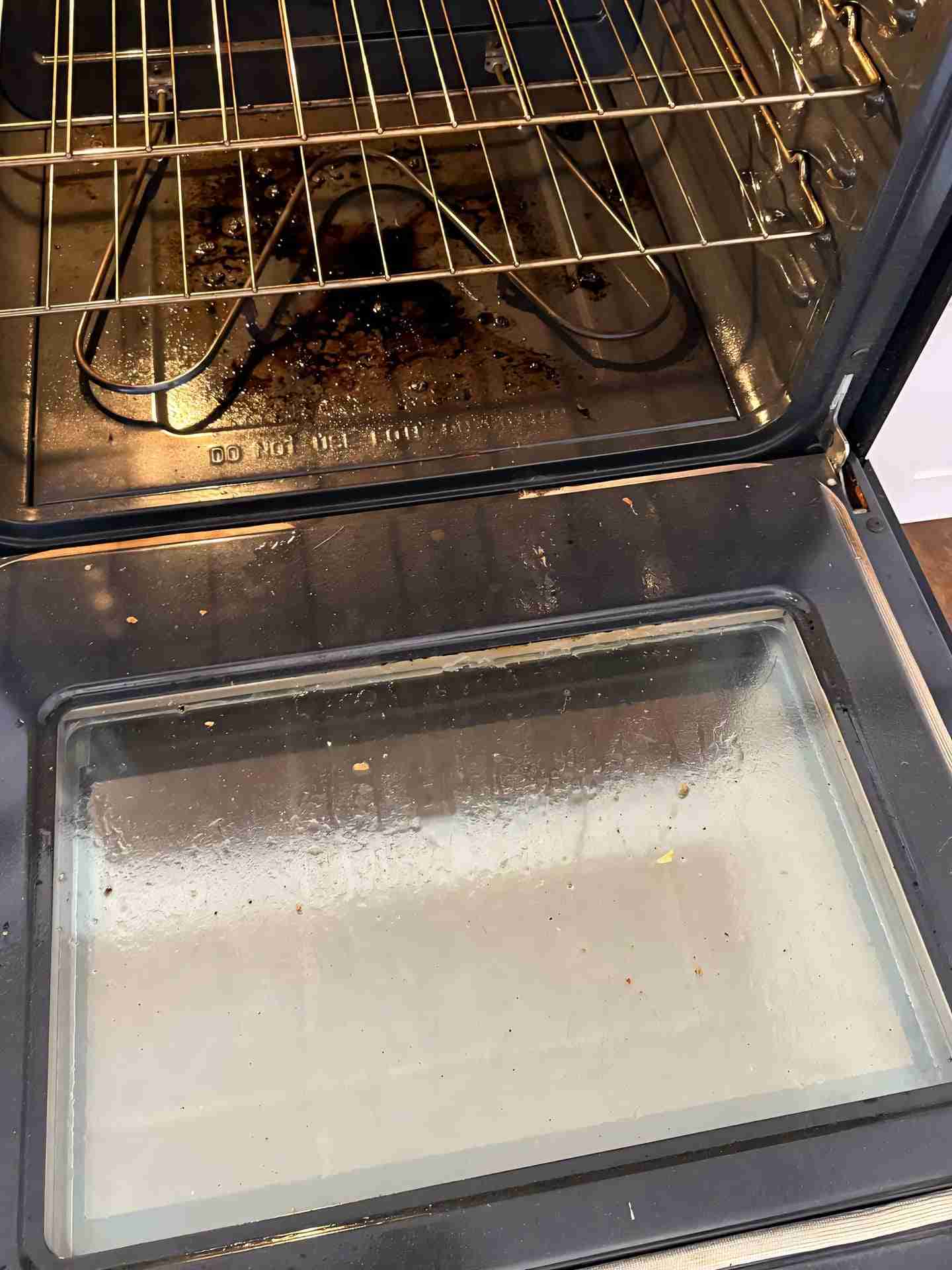 Close-up of a dirty oven door with burnt stains before cleaning.